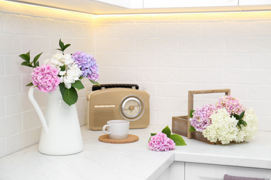 Beautiful hydrangea flowers, cup and radio set on light countertop