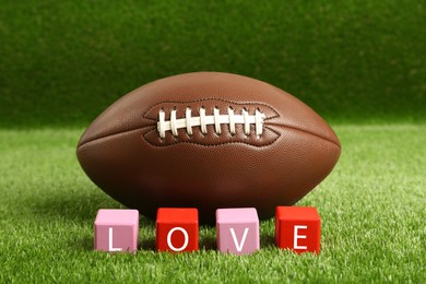 Photo of American football ball and cubes with word Love on green grass
