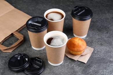 Photo of Coffee to go. Paper cups with tasty drink and muffin on grey table