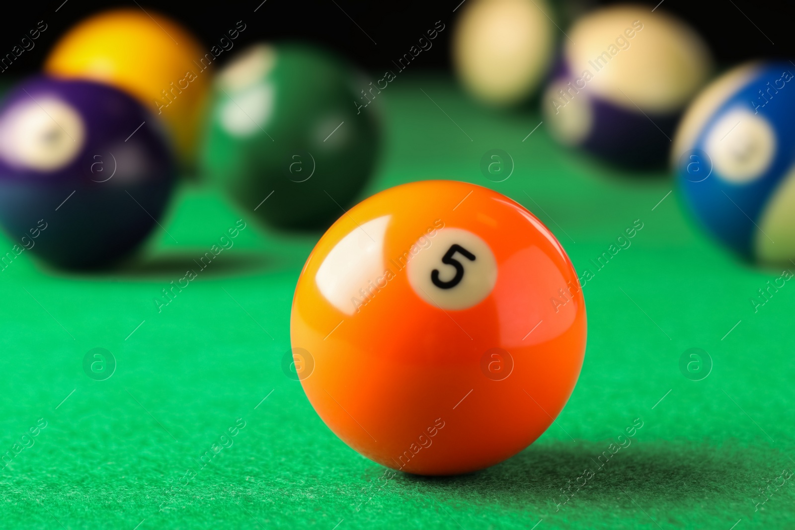 Photo of Billiard ball with number 5 on green table, closeup