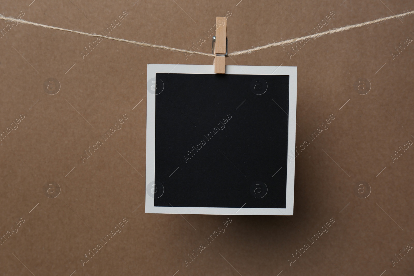 Photo of Wooden clothespin with empty instant frame on twine against brown background. Space for text