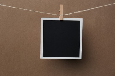 Photo of Wooden clothespin with empty instant frame on twine against brown background. Space for text