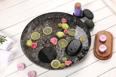 Photo of Plate with water, flowers, burning candles and lime slices on white wooden floor. Pedicure procedure