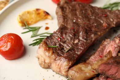 Photo of Delicious grilled beef steak, tomato, rosemary and lemon slice on plate, closeup