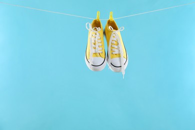 Photo of Stylish sneakers drying on washing line against light blue background, space for text