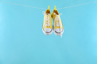 Stylish sneakers drying on washing line against light blue background, space for text