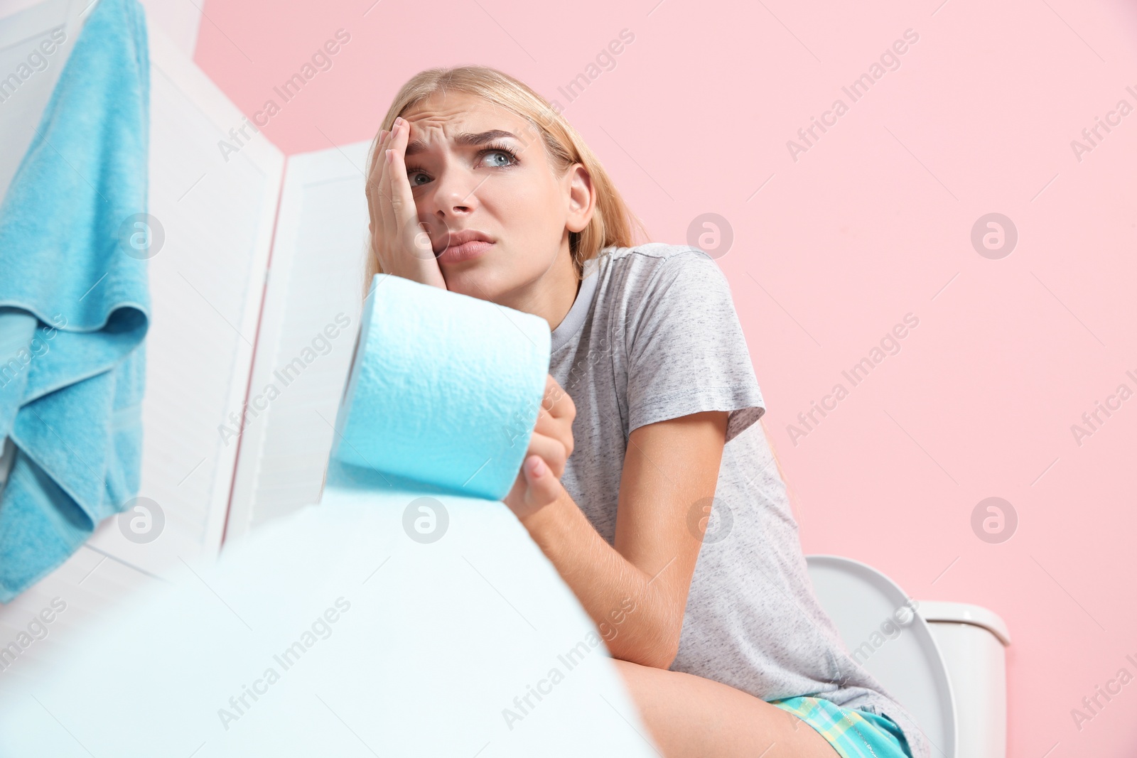 Photo of Woman with paper roll sitting on toilet bowl in bathroom