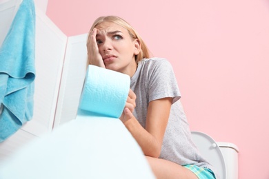 Woman with paper roll sitting on toilet bowl in bathroom