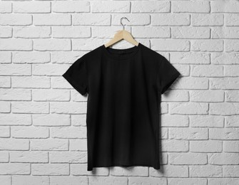 Hanger with stylish black T-shirt on white brick wall