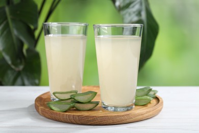 Photo of Fresh aloe juice in glasses and cut leaves on white wooden table outdoors