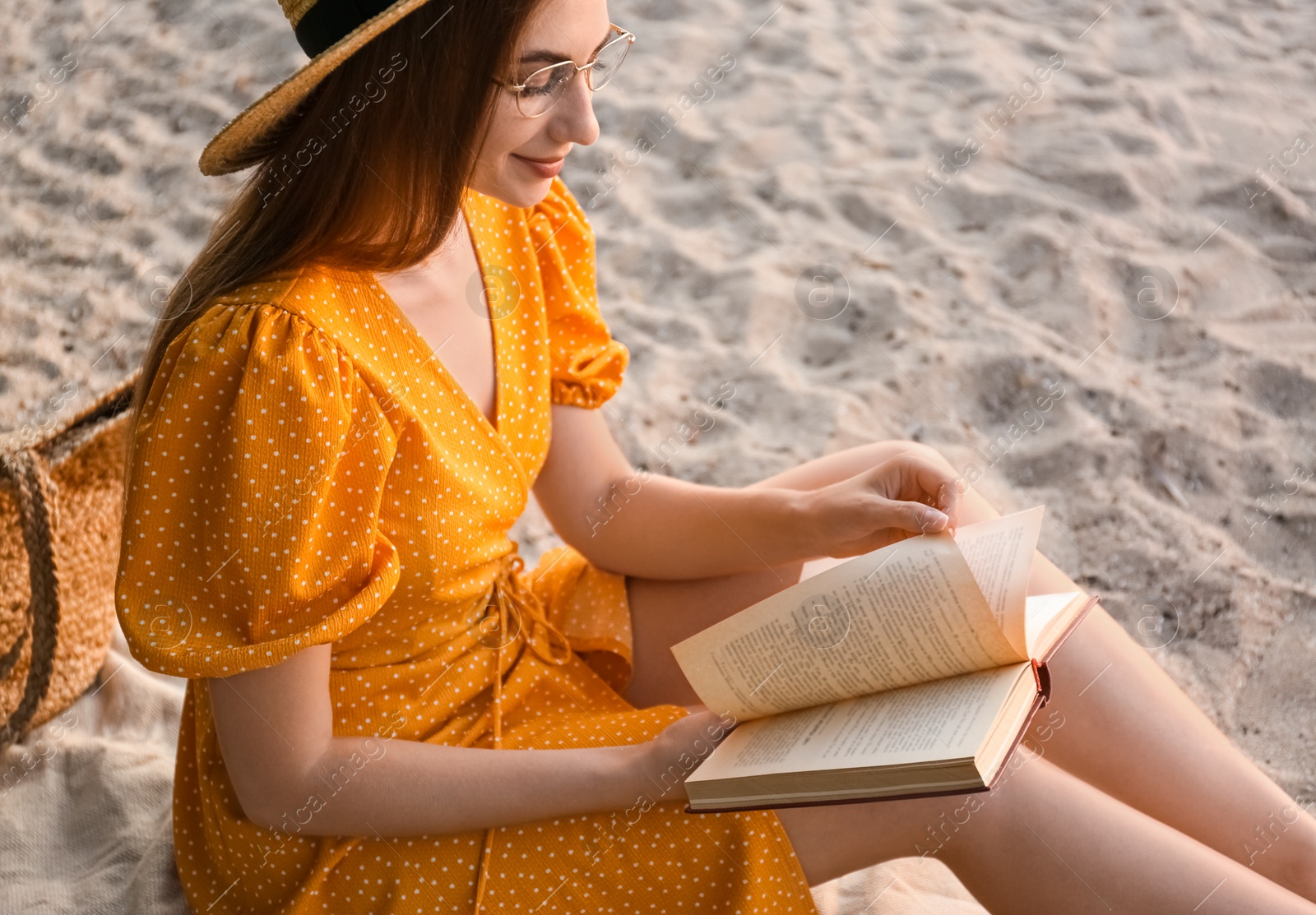 Photo of Young woman reading book on sandy beach