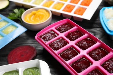 Photo of Different frozen purees in ice cube trays and ingredients of black wooden table. Ready for freezing