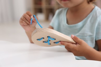 Photo of Motor skills development. Little girl playing with wooden lacing toy at table indoors, closeup