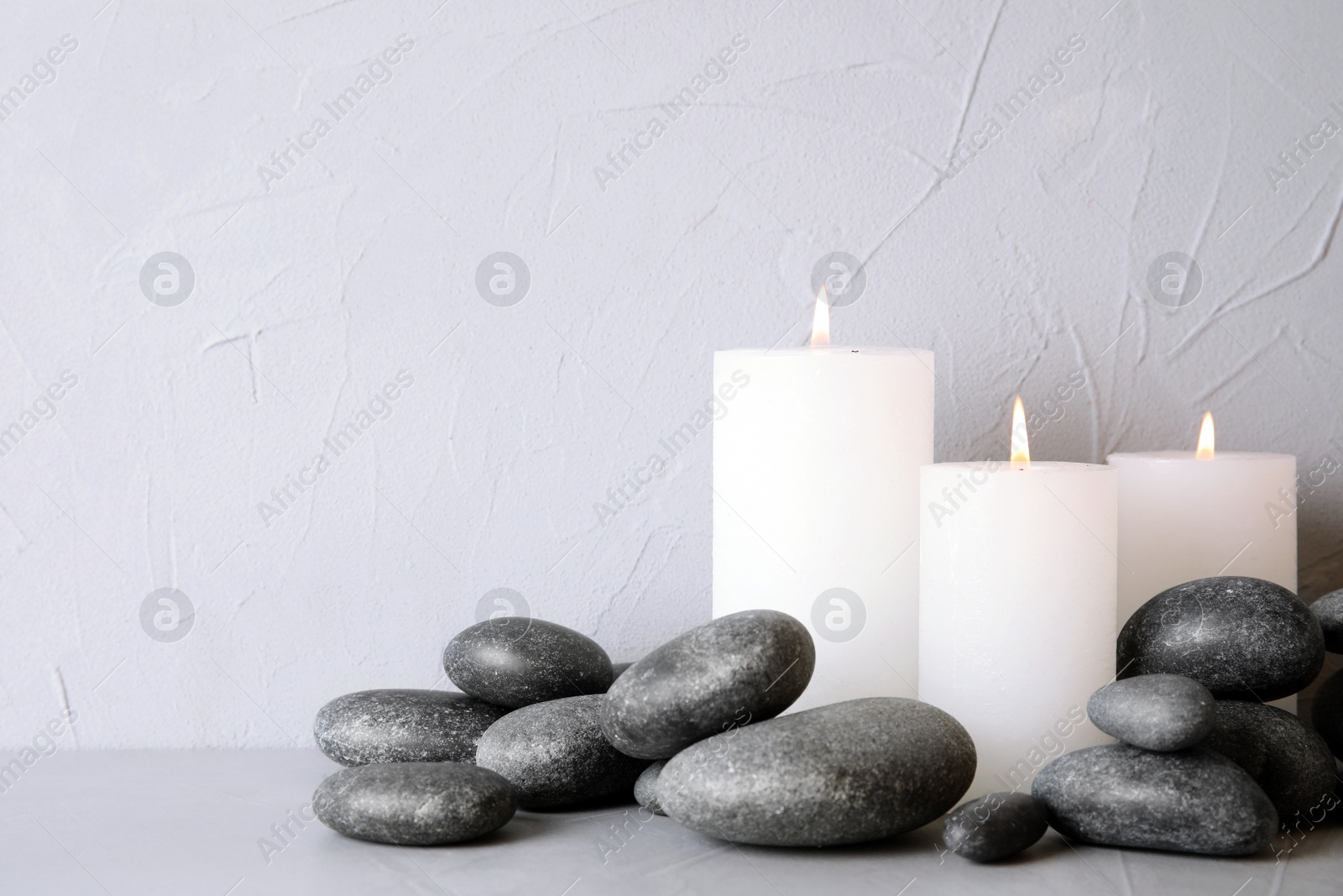 Photo of Zen stones and lighted candles on table against light background. Space for text