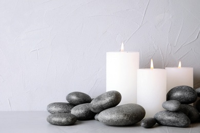 Zen stones and lighted candles on table against light background. Space for text