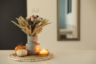 Beautiful bouquet of dry flowers, small pumpkins and candle on white table indoors, space for text