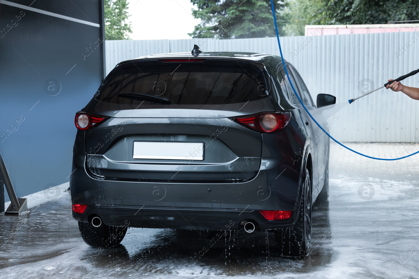 Photo of Man washing auto with high pressure water jet at car wash, closeup