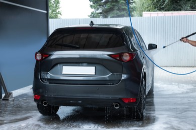 Photo of Man washing auto with high pressure water jet at car wash, closeup