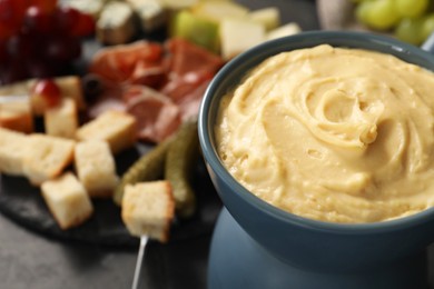 Fondue with tasty melted cheese, fork and different snacks on black table, closeup