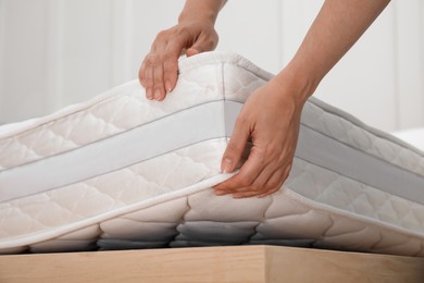 Photo of Woman putting soft white mattress on bed indoors, closeup