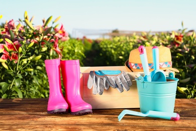 Photo of Rubber boots and gardening tools on wooden table at lily field