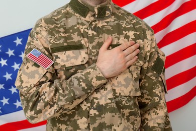 Photo of Soldier holding hand on heart near United states of America flag on white background, closeup