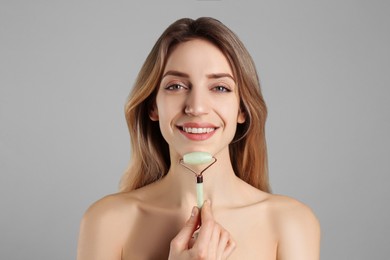 Photo of Young woman using natural jade face roller on light grey background