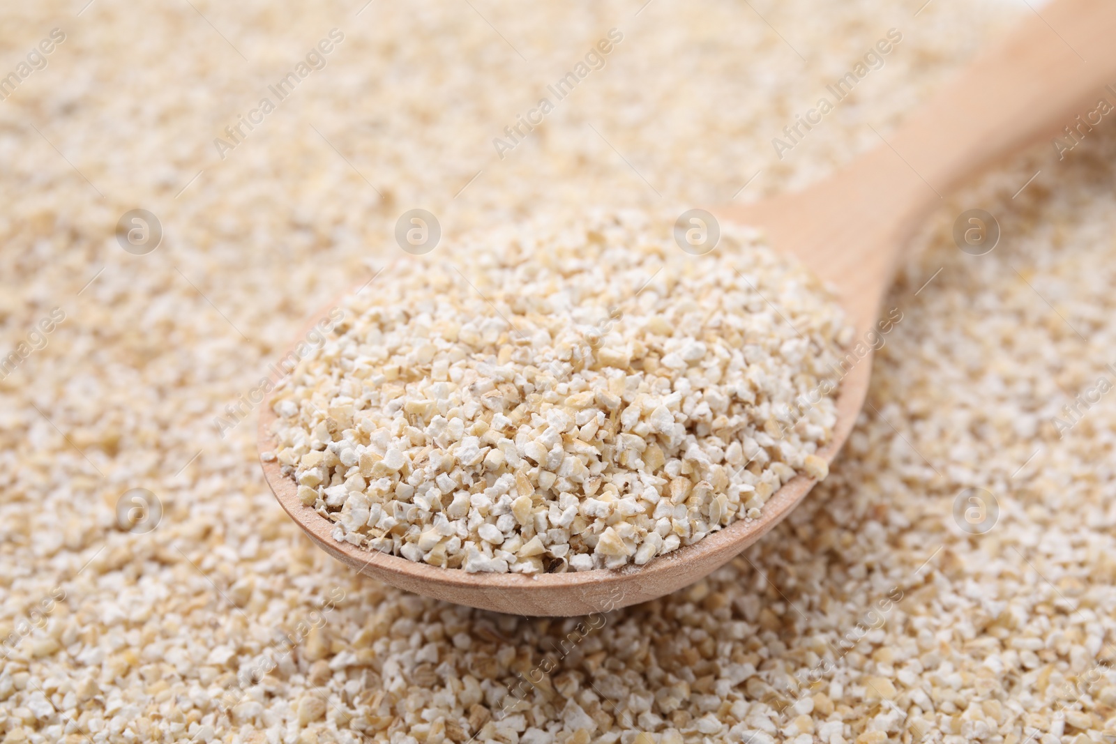 Photo of Wooden spoon on raw barley groats, closeup