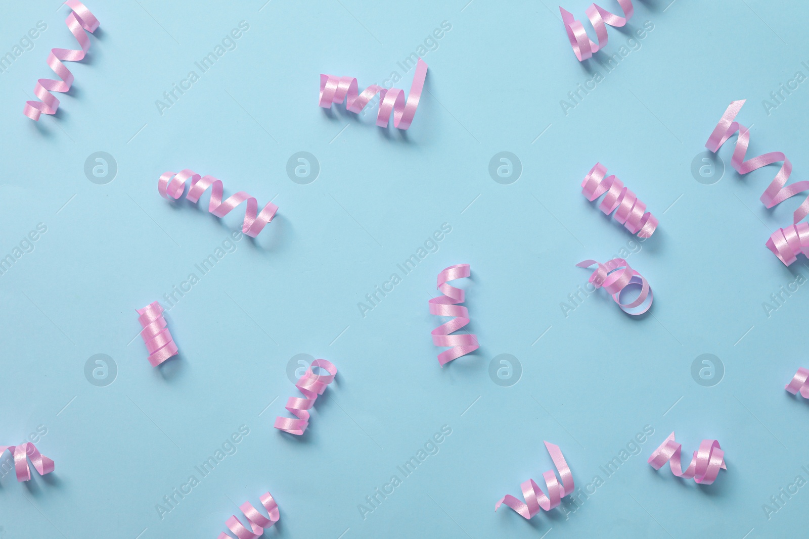 Photo of Shiny pink serpentine streamers light blue background, flat lay