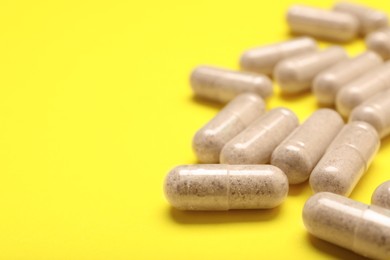 Many transparent gelatin capsules on yellow background, closeup. Space for text