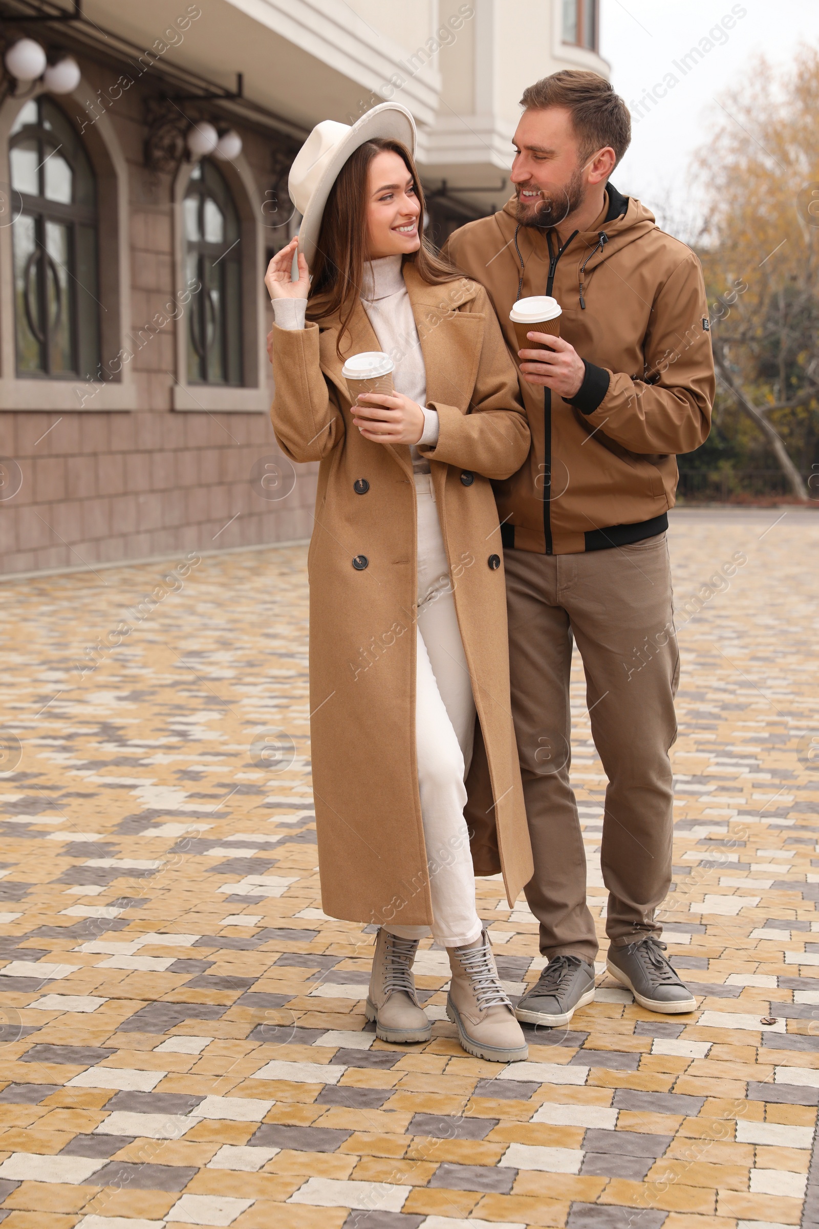 Photo of Happy couple wearing stylish autumn clothes with cups of coffee on city street