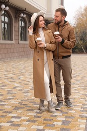 Happy couple wearing stylish autumn clothes with cups of coffee on city street