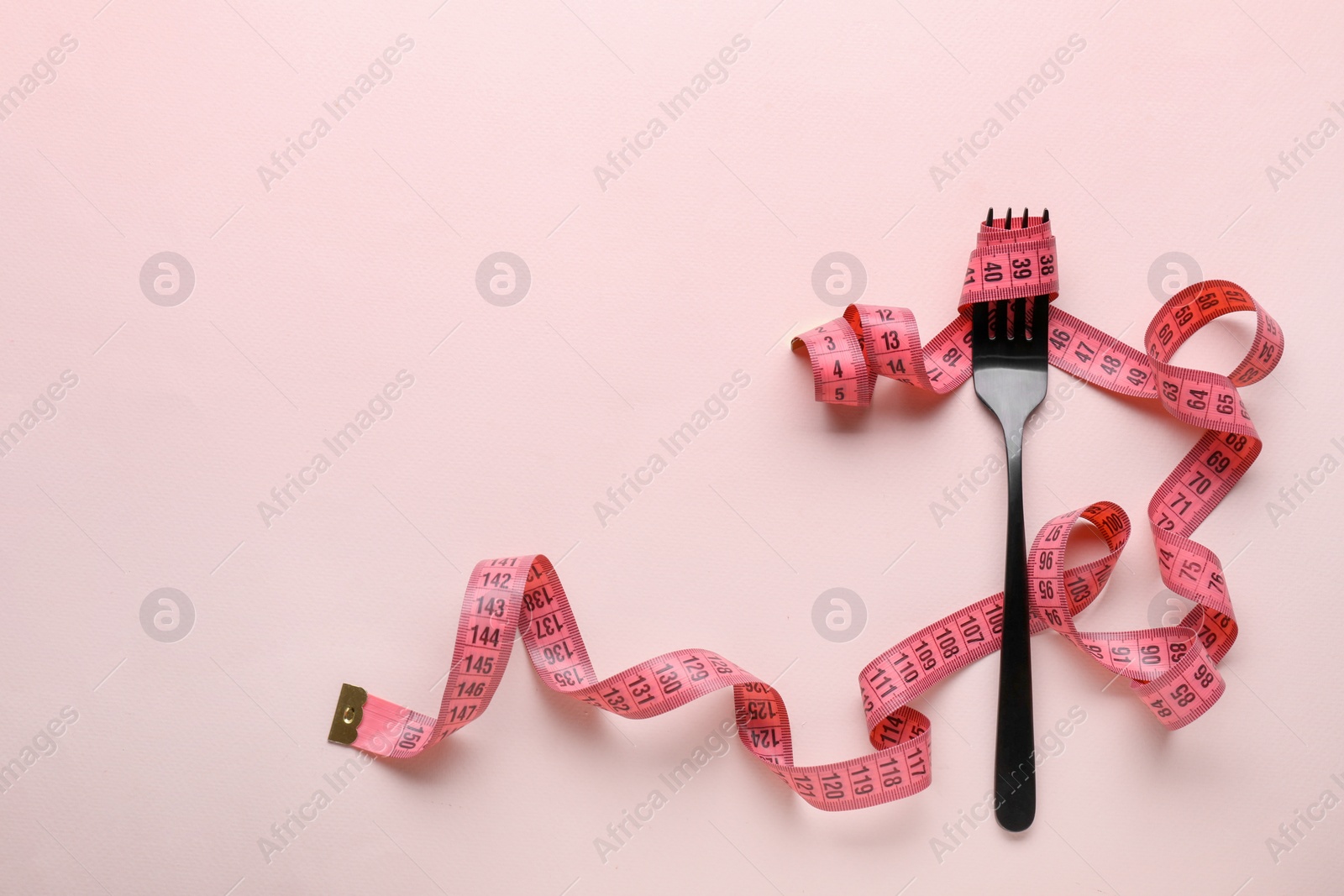 Photo of Fork with measuring tape on pale pink background, top view and space for text. Diet concept