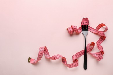 Fork with measuring tape on pale pink background, top view and space for text. Diet concept