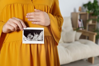 Photo of Pregnant woman with ultrasound picture of baby in living room, closeup. Space for text