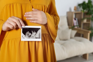 Pregnant woman with ultrasound picture of baby in living room, closeup. Space for text