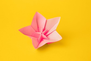 Origami art. Handmade pink paper flower on yellow background, above view