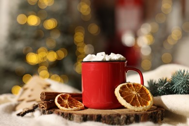 Photo of Cup of cocoa with marshmallows, cinnamon sticks, dry orange slices and Christmas decor on table against festive lights, closeup