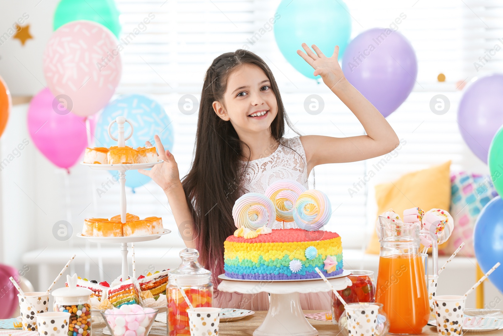 Photo of Happy girl at table with treats in room decorated for birthday party