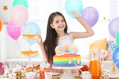 Photo of Happy girl at table with treats in room decorated for birthday party