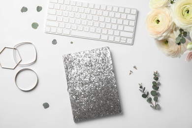 Flat lay composition with glittering notebook, keyboard and spring flowers on white background