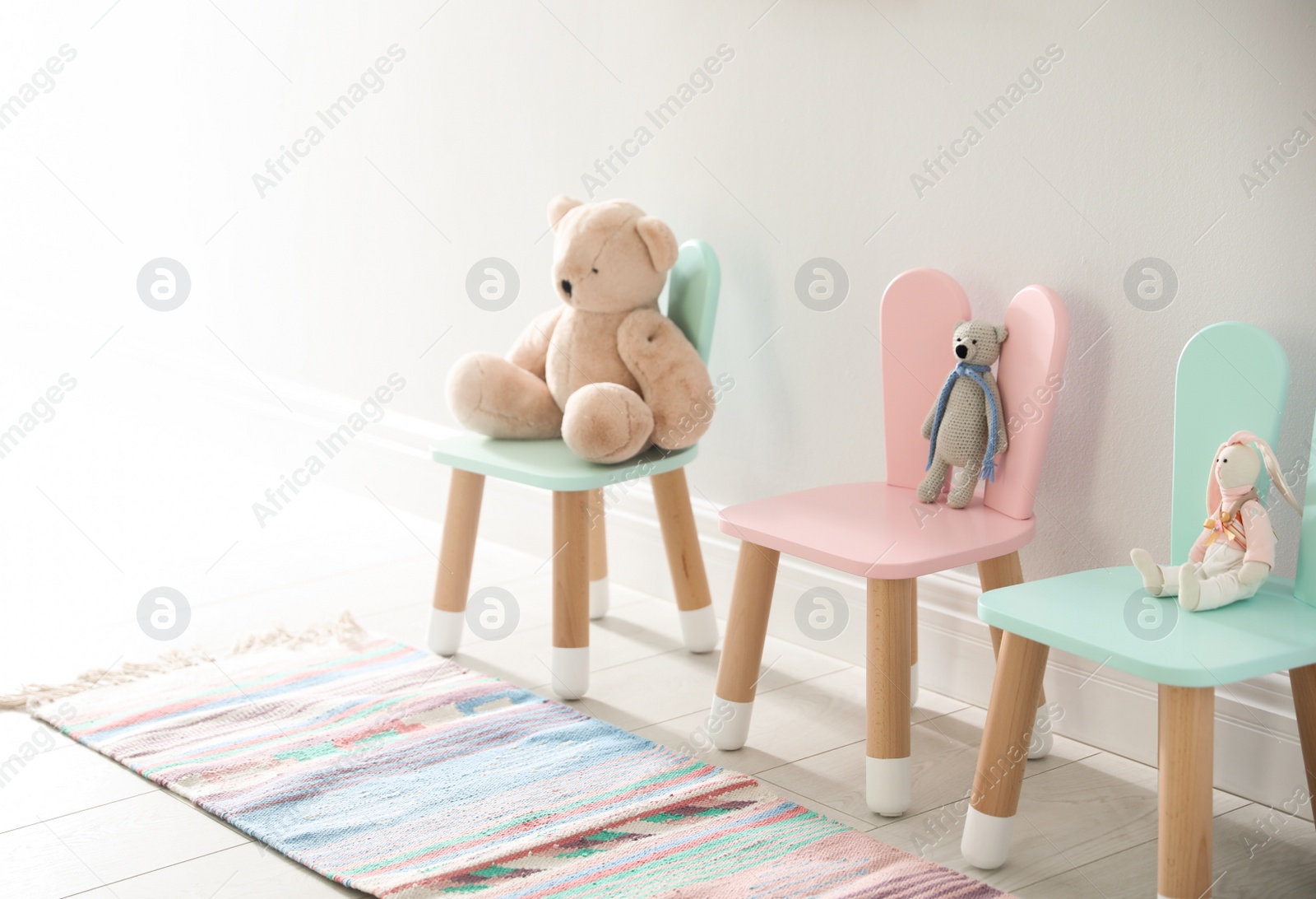 Photo of Cute toys on chairs with bunny ears near white wall indoors. Children's room interior