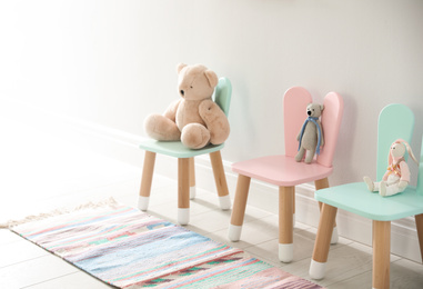 Photo of Cute toys on chairs with bunny ears near white wall indoors. Children's room interior