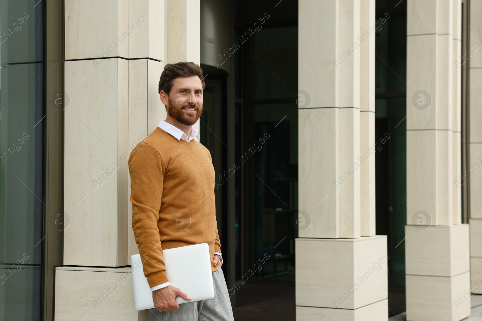 Photo of Handsome man with laptop near building on city street