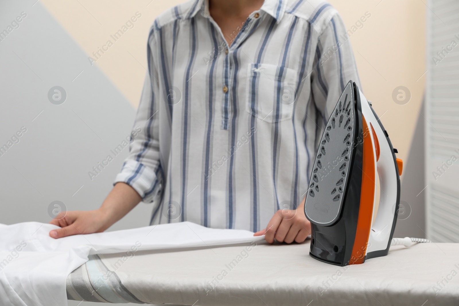 Photo of Woman ironing clean shirt on board against color background, closeup with space for text. Laundry day