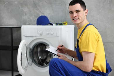 Photo of Smiling plumber writing results of examining washing machine in bathroom