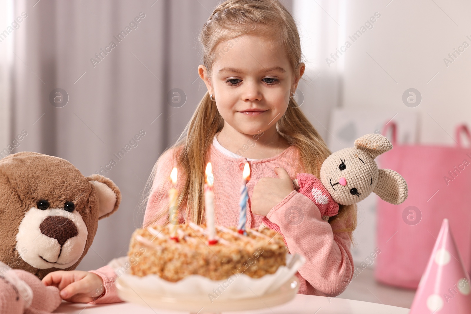 Photo of Cute girl with birthday cake and toys at table indoors