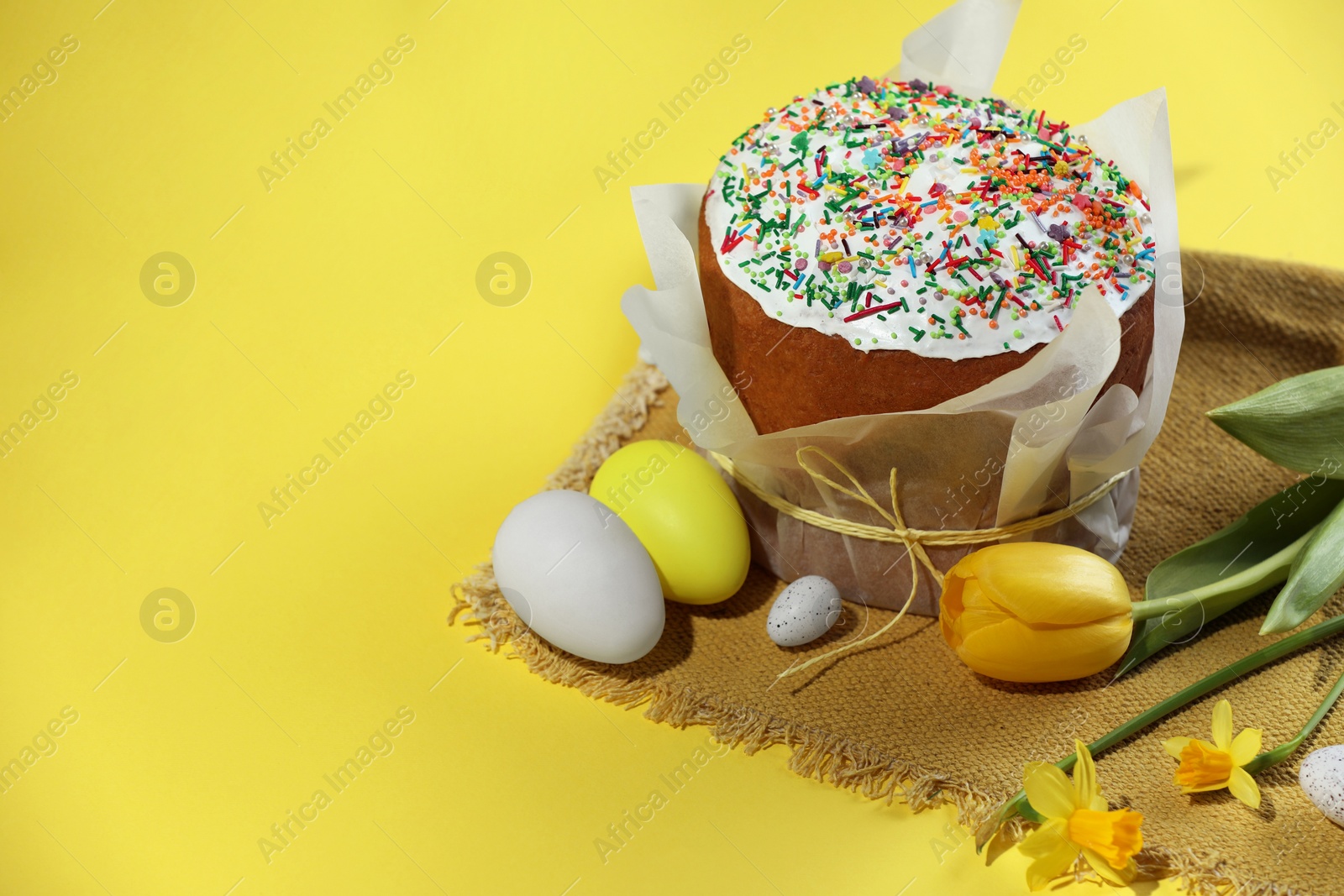 Photo of Traditional Easter cake with sprinkles, decorated eggs and flowers on yellow background. Space for text