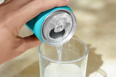 Woman pouring drink from aluminum can into glass on blurred background, closeup