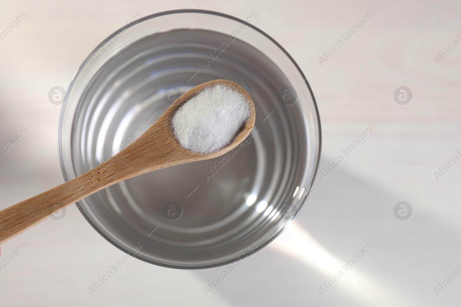 Photo of Spoon with baking soda over glass of water on light background, top view. Space for text